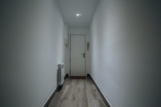 Biele dvere na konci dlhej úzkej chodby s drevenou podlahou