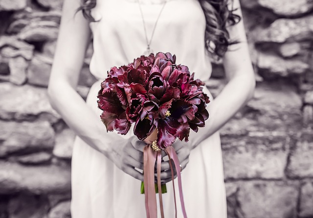 Žena v bielych šatách pred sebou drží kyticu červených kvetov.jpg