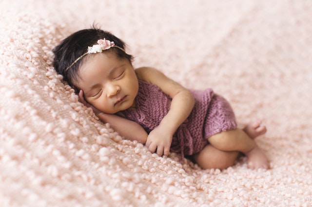 Malé bábätko v ružových štrikovaných šatách spí.jpg